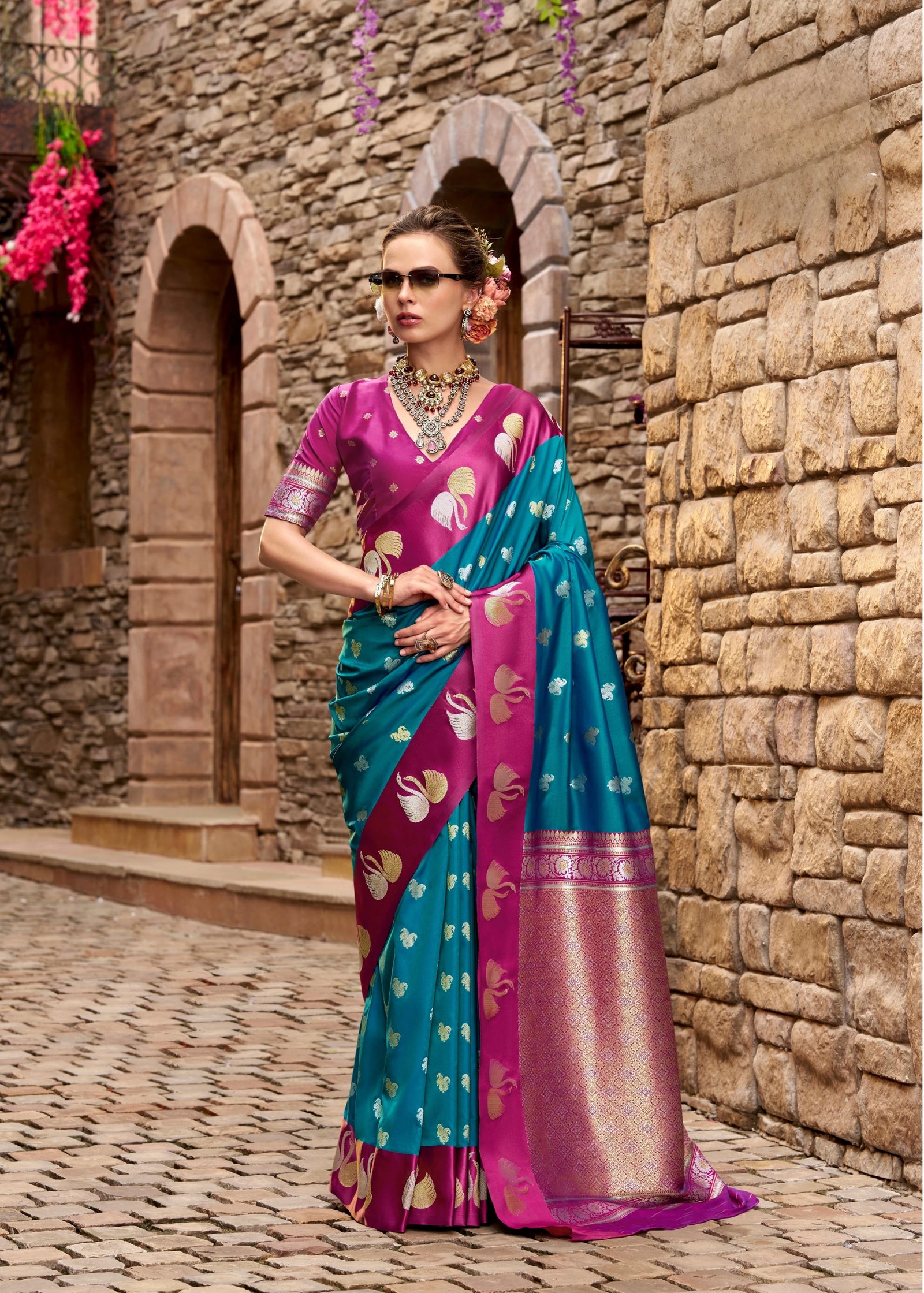 Woman in a colorful saree standing against a stone wall.