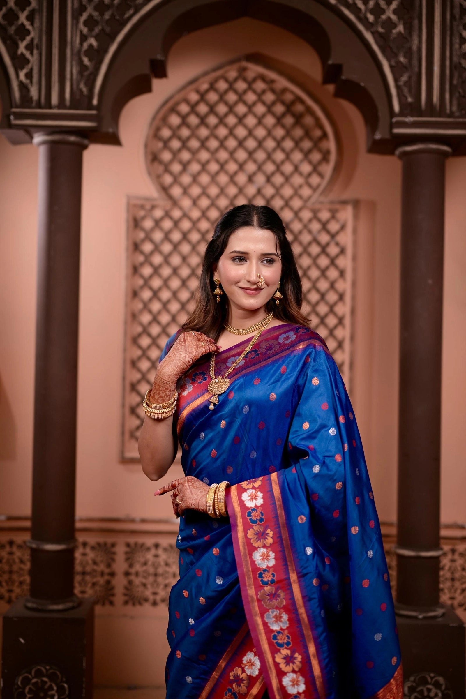 Woman in a blue saree with floral patterns standing in front of an ornate archway.
