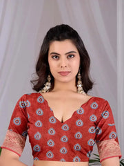 A woman wearing a rust red cotton blouse with a blue and white paisley pattern and lace sleeve cuffs, set against a soft white draped fabric background.