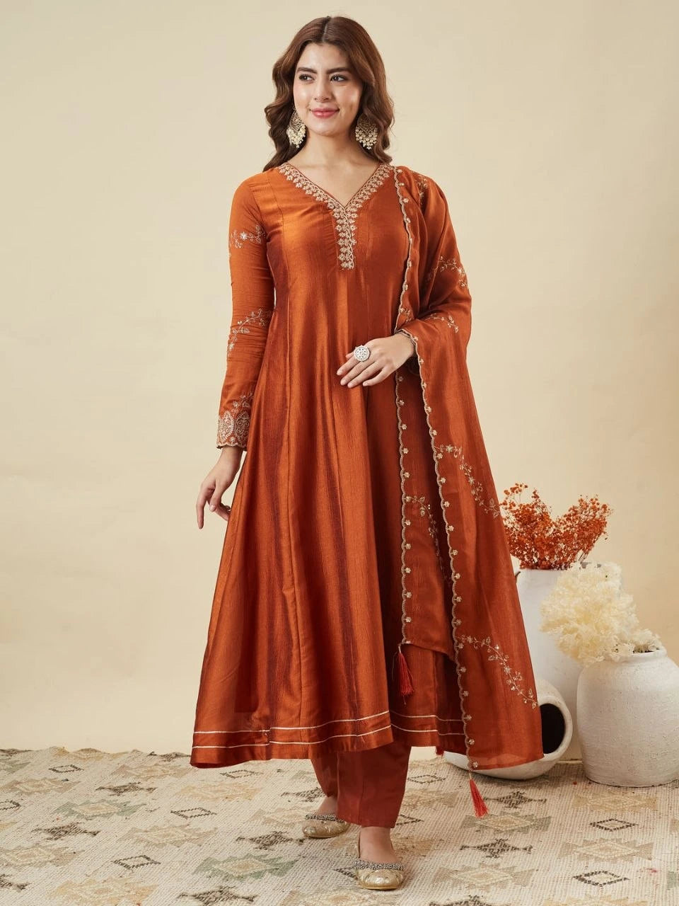 Woman wearing a rust-colored traditional outfit with intricate designs on a beige background