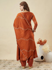 Woman wearing an orange traditional outfit with floral patterns, standing against a beige background.