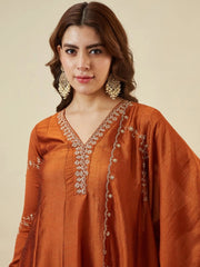 Woman wearing an orange embroidered traditional outfit against a beige background