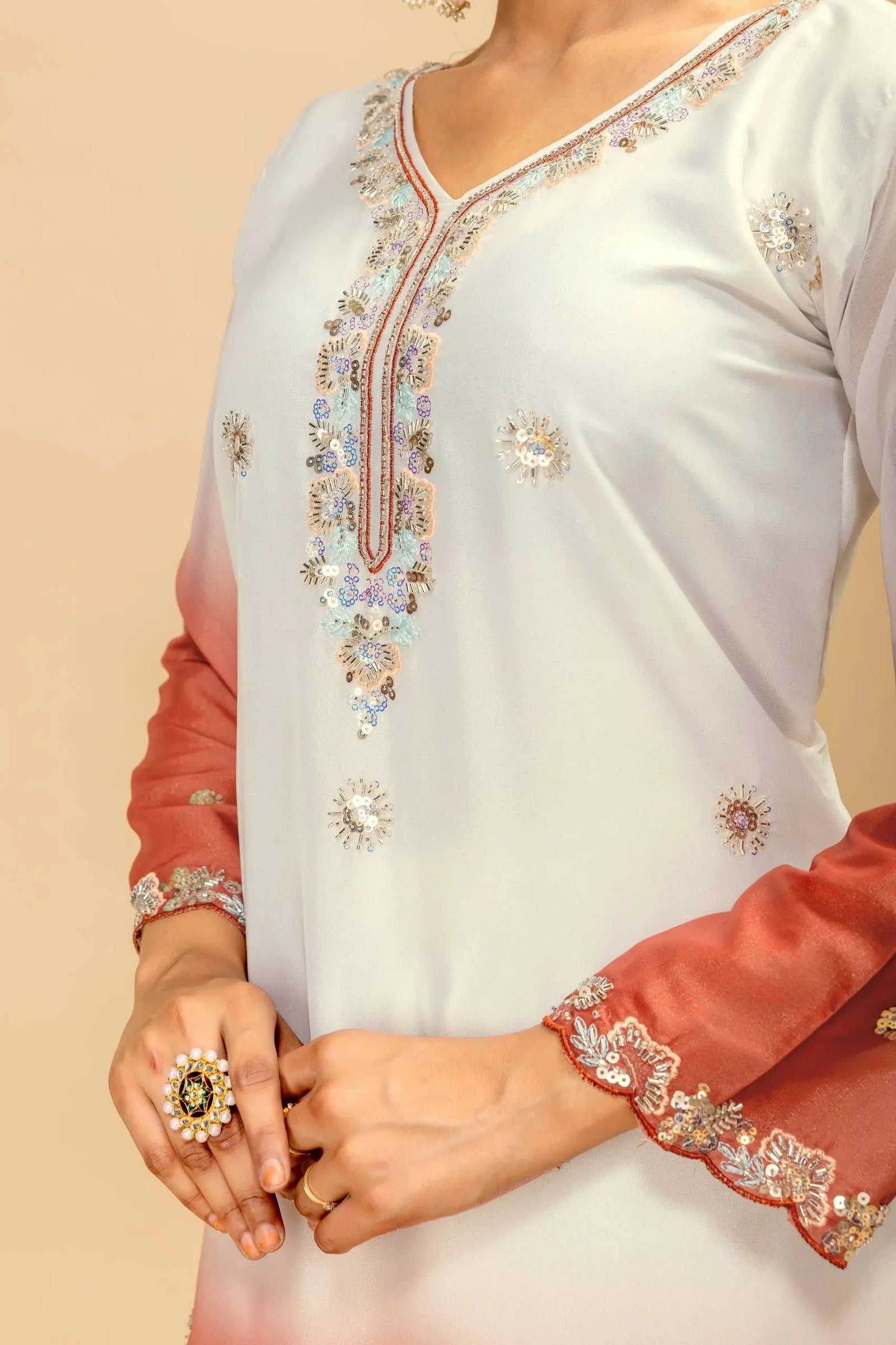 Close-up of a white and peach traditional outfit with intricate embroidery on a beige background