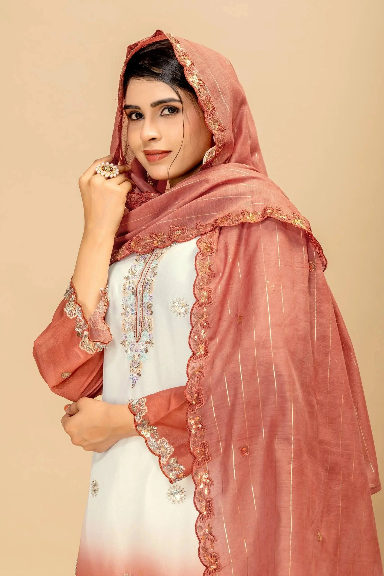 Woman wearing a white outfit with a pink embroidered dupatta against a beige background