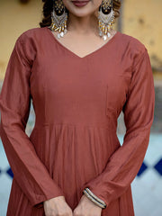 Person wearing a rust-colored dress with long sleeves and a blurred background