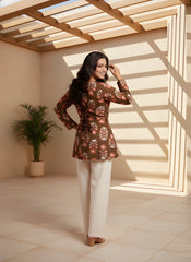 Woman in a patterned top and white pants standing in a sunlit room with wooden beams.