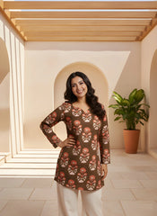 Woman wearing a patterned top in a well-lit room with a plant in the background