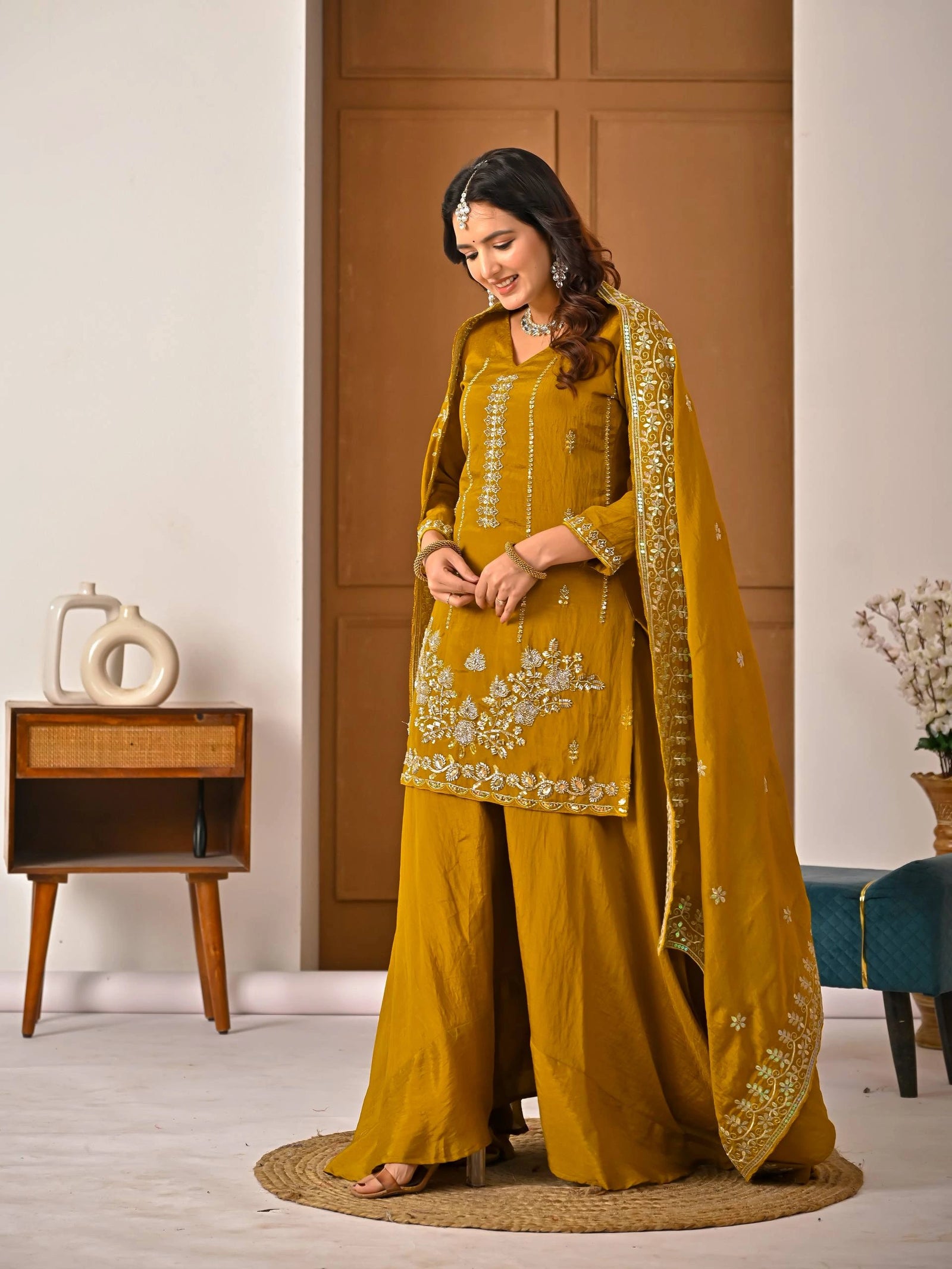 Woman in a mustard yellow traditional outfit with embroidery in a room setting.