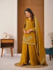 Woman in a mustard yellow traditional outfit with embroidery in a room setting.