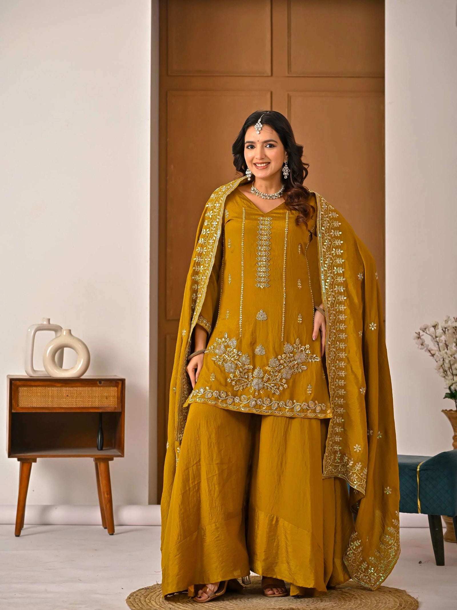 Woman in a mustard yellow traditional outfit with embroidery in a room setting.