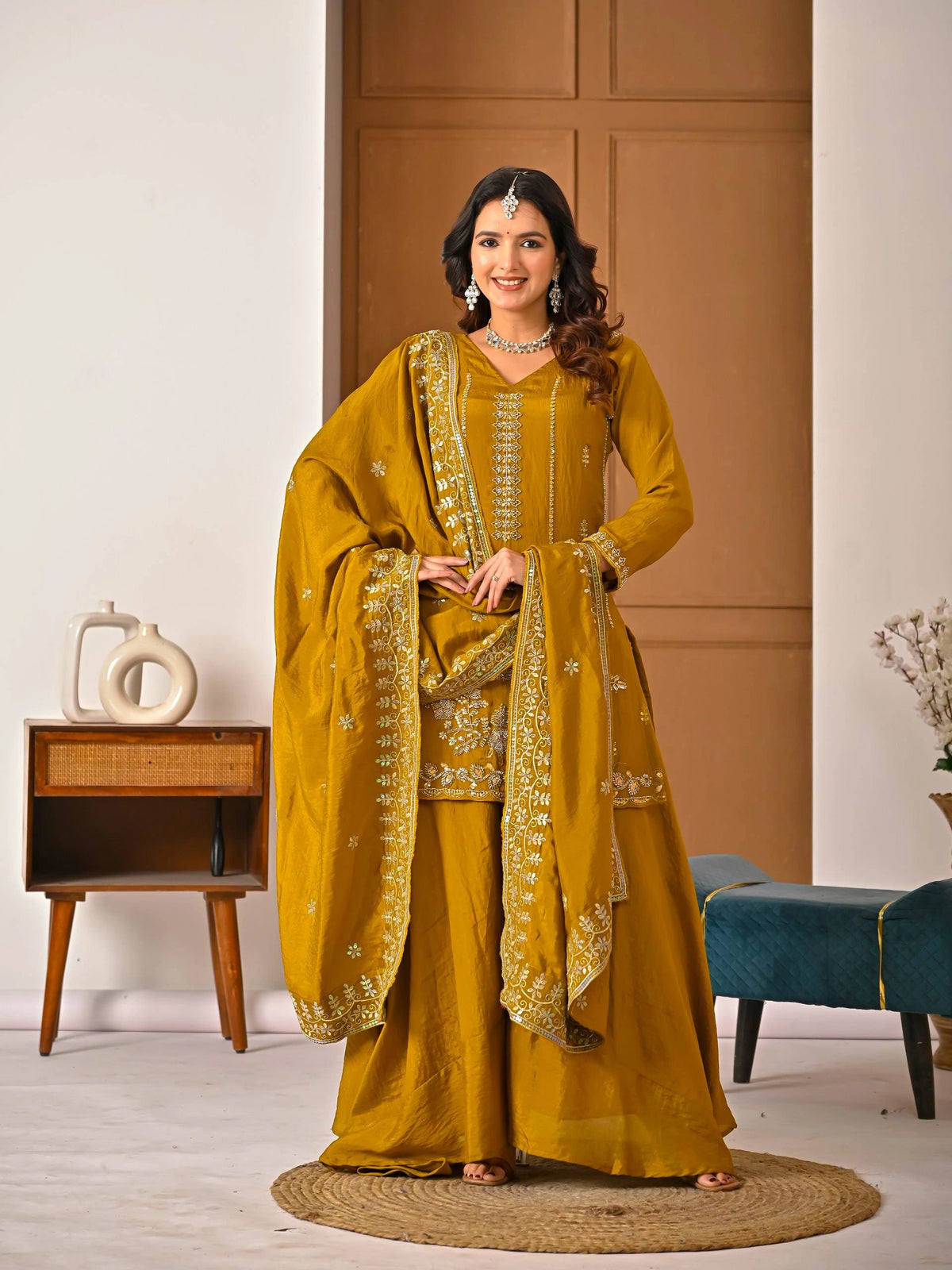 Woman in a mustard yellow traditional outfit with embroidery in a room setting.