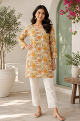 Woman wearing a floral kurta with white pants in an indoor setting with plants and a wooden stool.