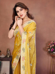 Woman wearing a yellow saree with floral patterns against a brown background
