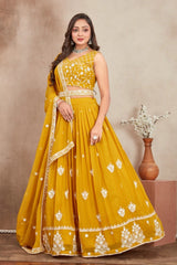 Woman wearing a yellow embroidered saree with a plain background