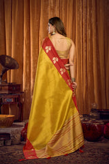 Woman in a yellow saree with red border standing in front of a wooden curtain.
