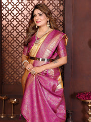 Woman in a pink saree with gold border against a decorative wall.