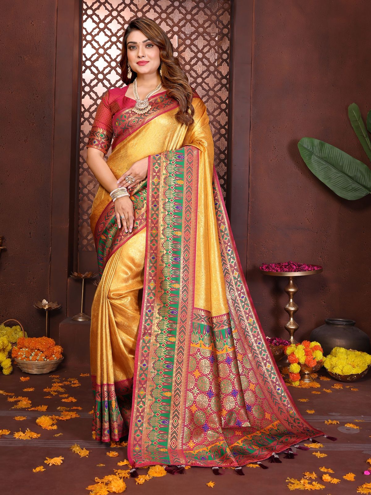Woman wearing a traditional yellow saree with a colorful border against a decorative background.