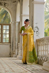 Woman in a yellow and green saree standing in an elegant indoor setting.