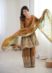 Woman in traditional embroidered outfit with a green dupatta against a white curtain background