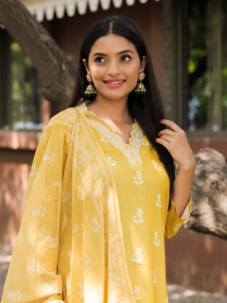 Woman wearing a yellow traditional outfit with a floral pattern, standing outdoors.