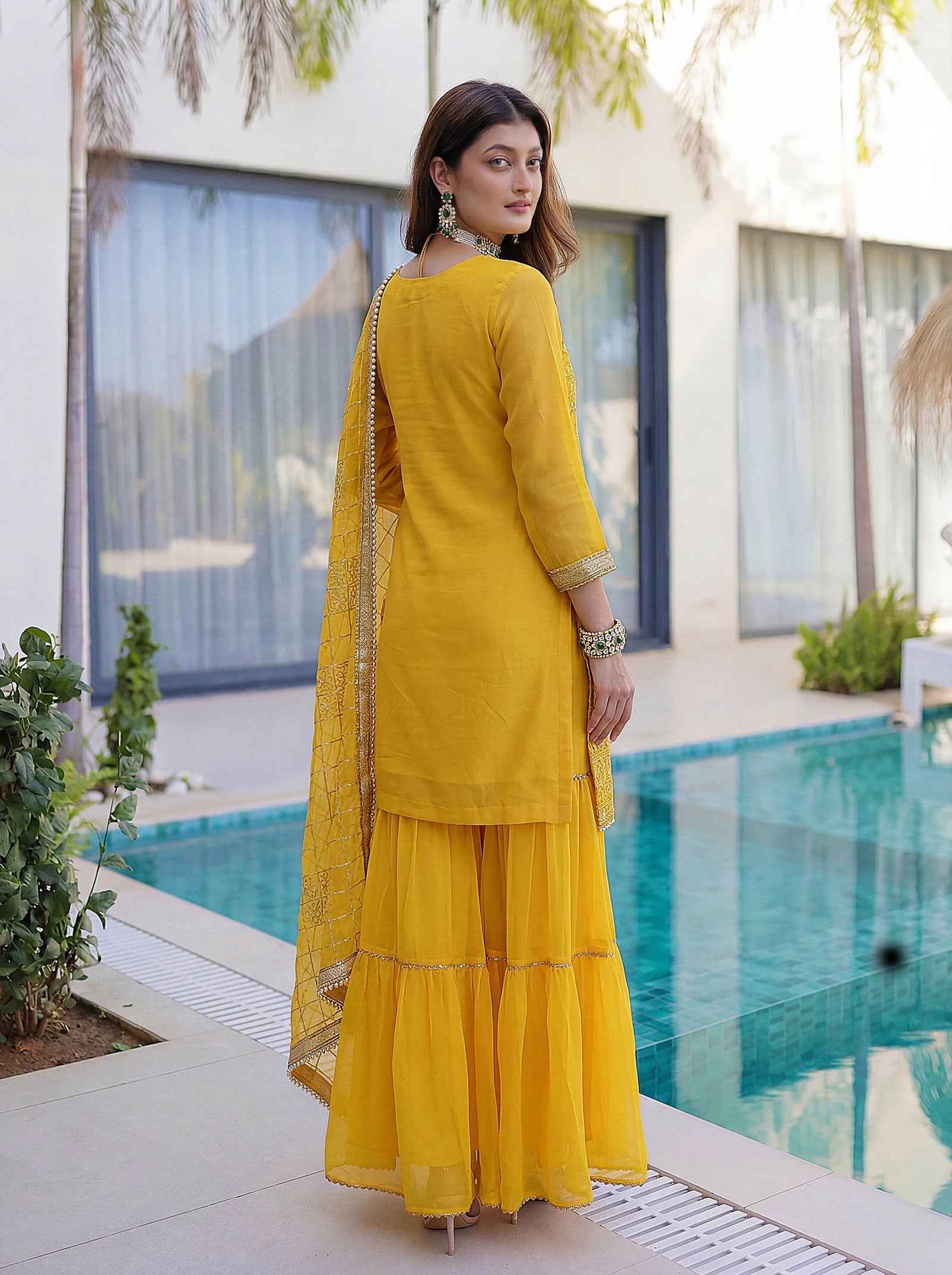 Woman in a yellow traditional outfit standing by a poolside.