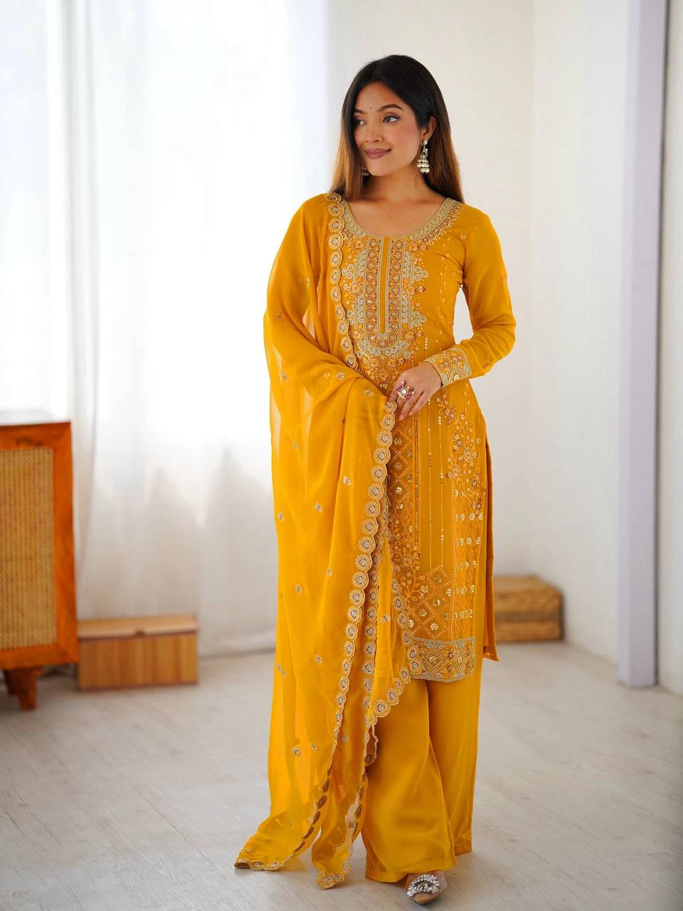 Woman wearing a yellow traditional outfit with intricate patterns in a bright room.