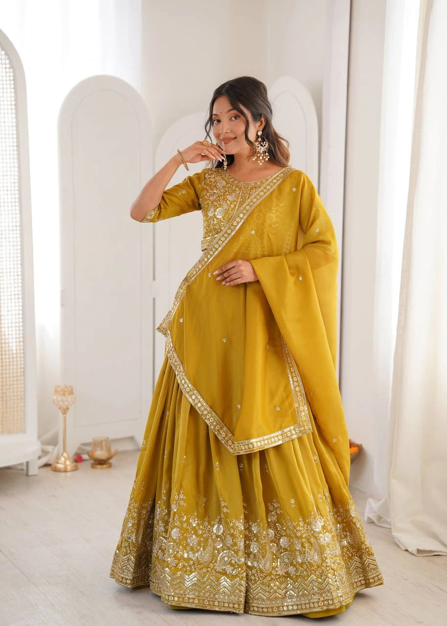 Woman in a yellow traditional outfit with gold embroidery standing in a bright room.