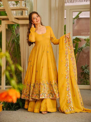 Woman in a yellow traditional outfit with a floral dupatta, standing indoors.