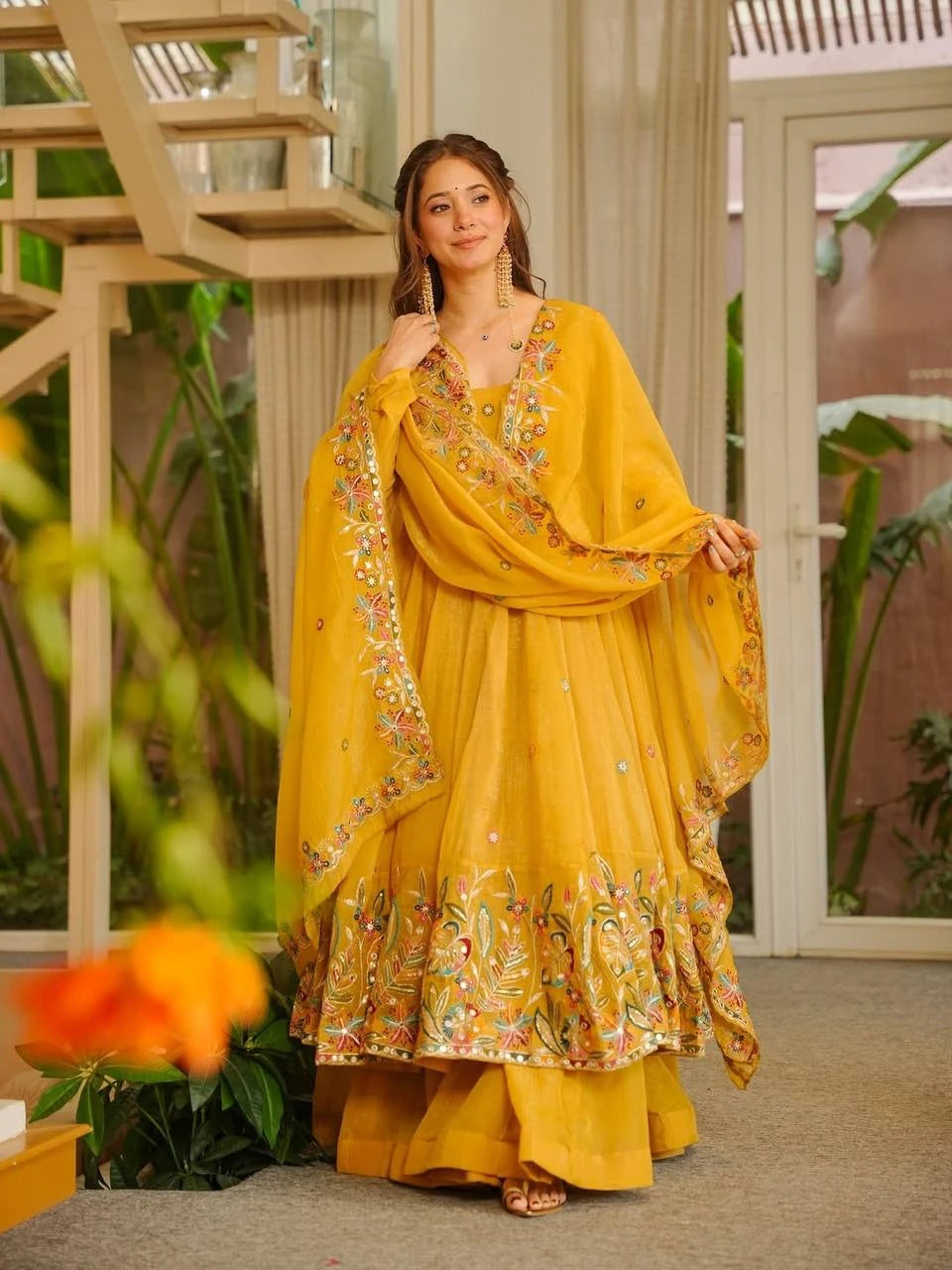 Woman in a yellow traditional outfit with floral patterns indoors.