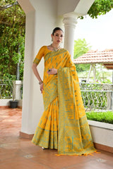 Woman in a yellow saree standing outdoors with greenery in the background