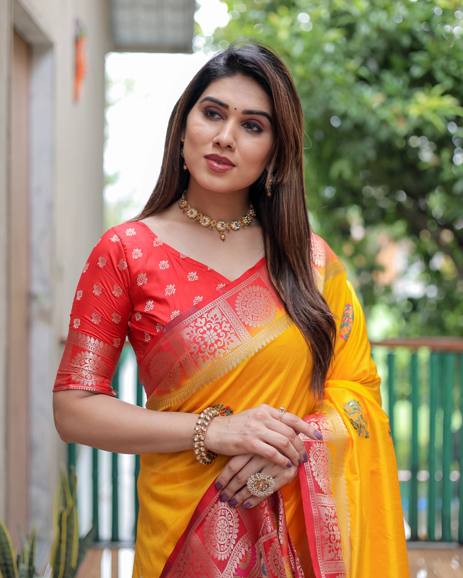 Woman wearing a red and yellow saree with a blurred outdoor background
