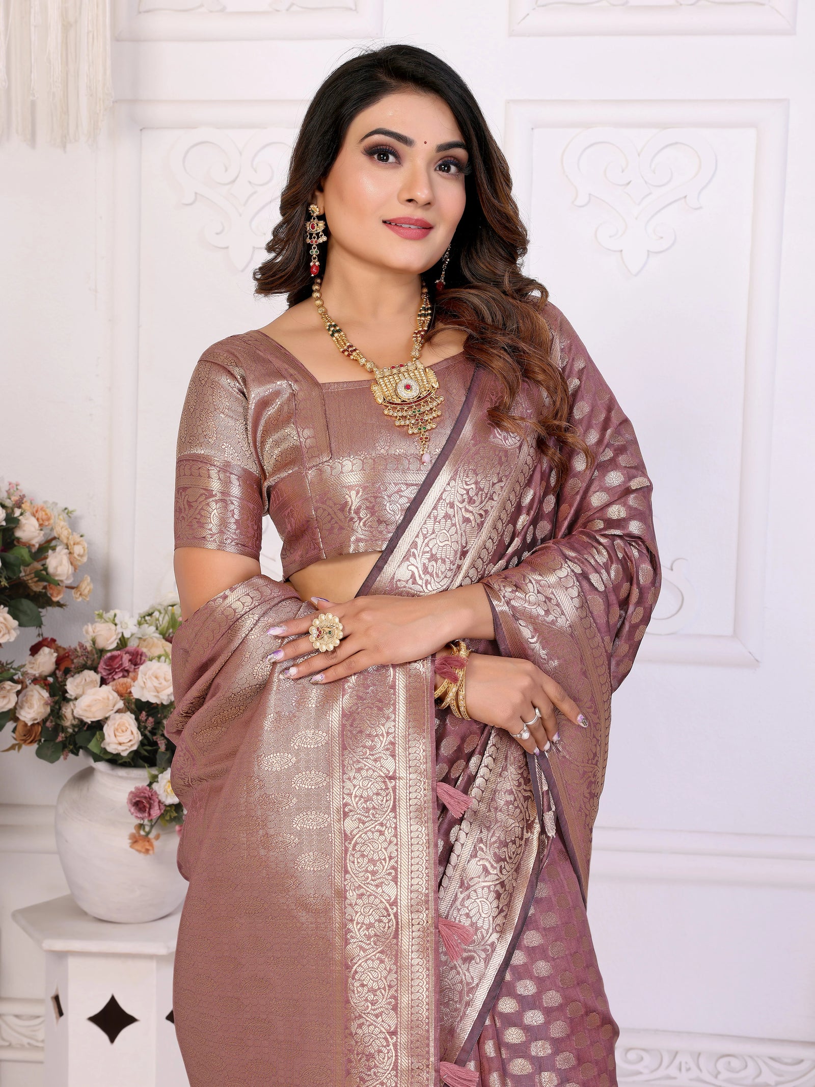 Woman wearing a traditional saree with a white decorative wall in the background