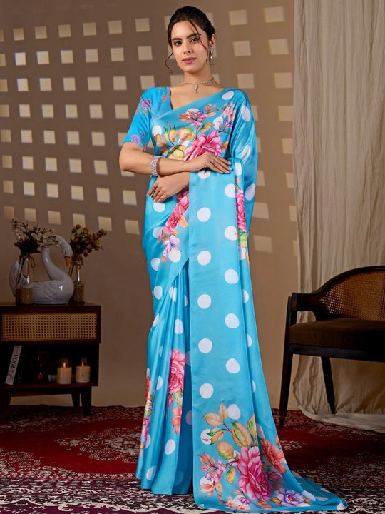 Woman wearing a blue saree with floral patterns in a room setting.