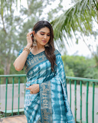 Woman wearing a blue tie-dye saree with a blurred green outdoor background