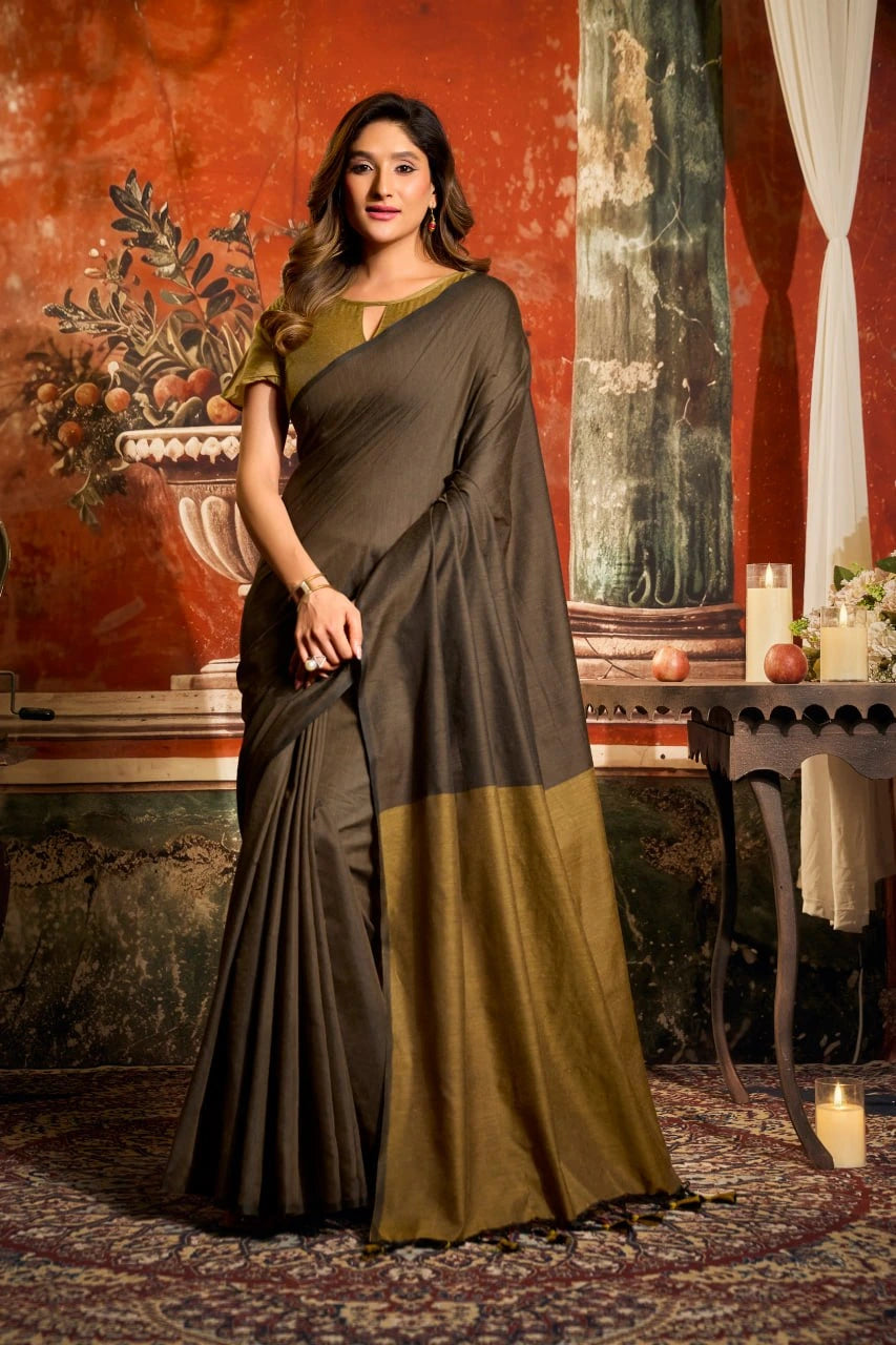 Woman in a dark gray and green saree standing in an ornate room with red walls and decorative elements.