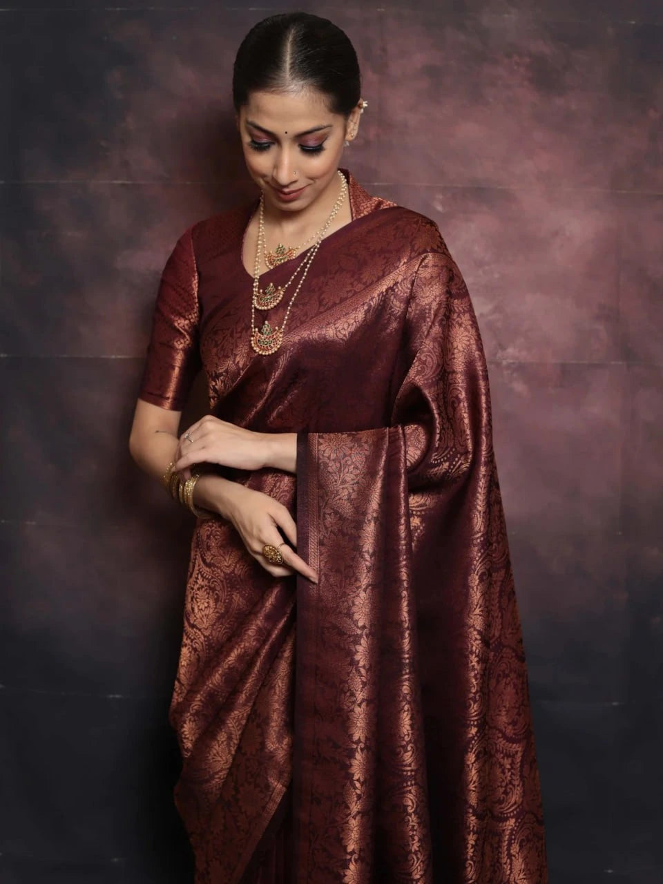 Woman wearing a maroon saree with a textured pattern against a dark background