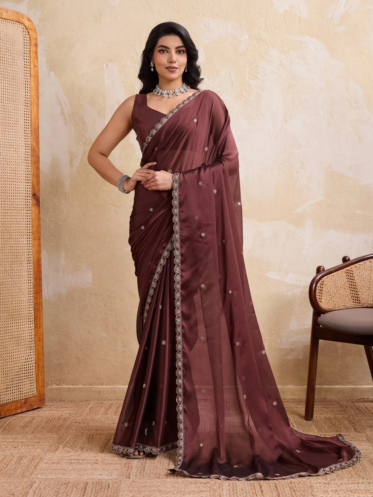 Woman wearing a maroon saree with a beige wall and chair in the background