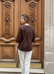 Woman in a brown top and white pants standing in front of an ornate wooden door.