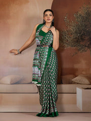Woman in a green and white patterned saree standing in a room with beige walls and furniture.