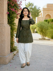 Woman in traditional outfit standing outdoors with greenery and architecture in the background