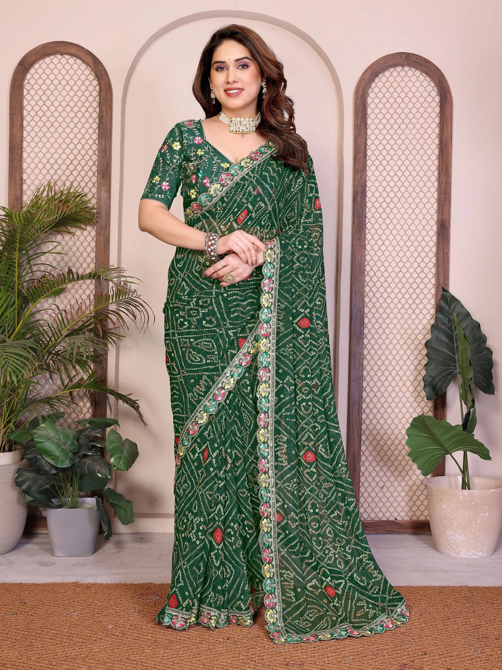 Woman wearing a green saree with floral patterns in a decorative setting with plants.