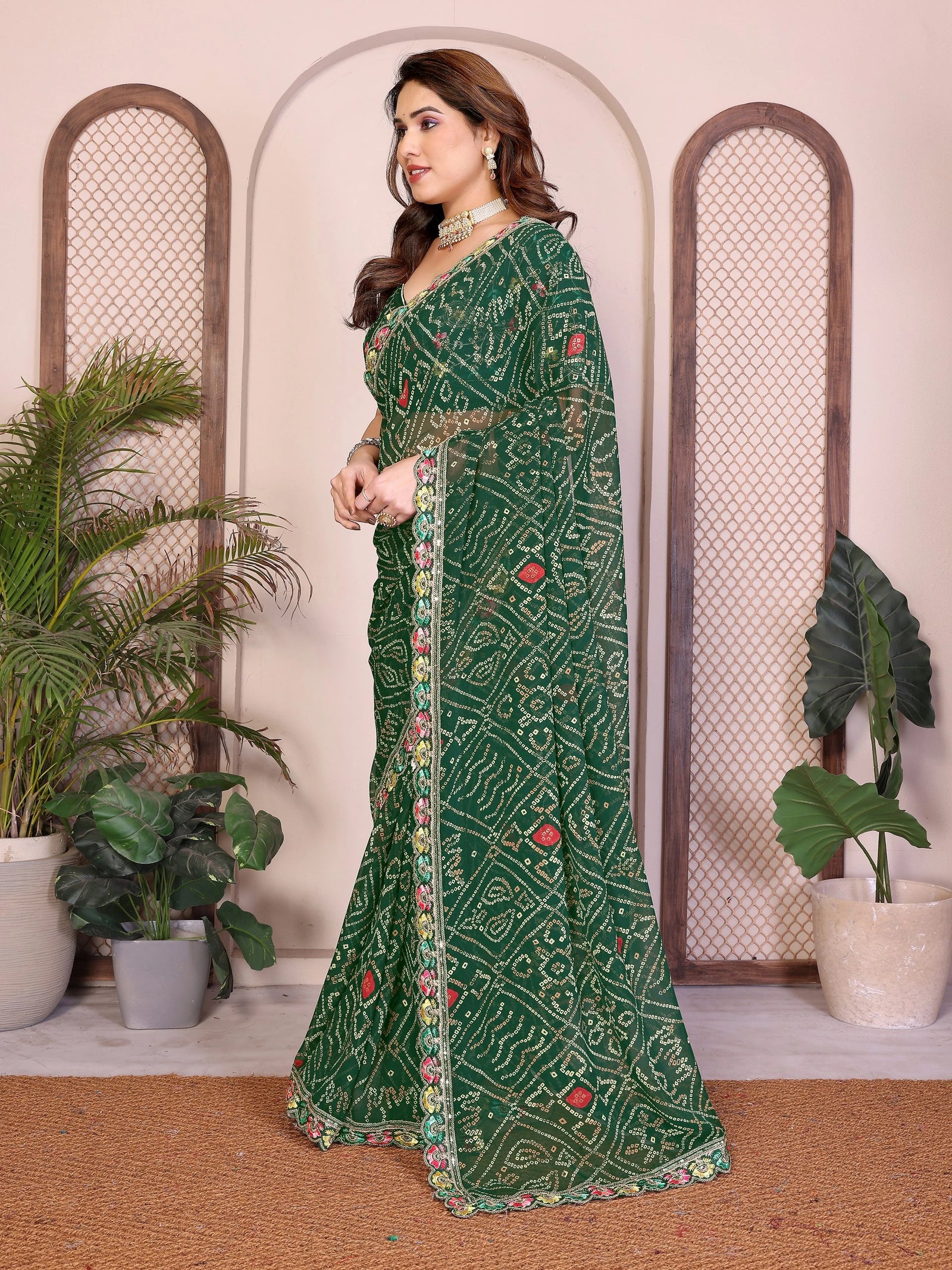 Woman wearing a green saree with a pattern in a decorated room with plants.