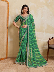 Woman wearing a green saree with a patterned border against a beige wall.