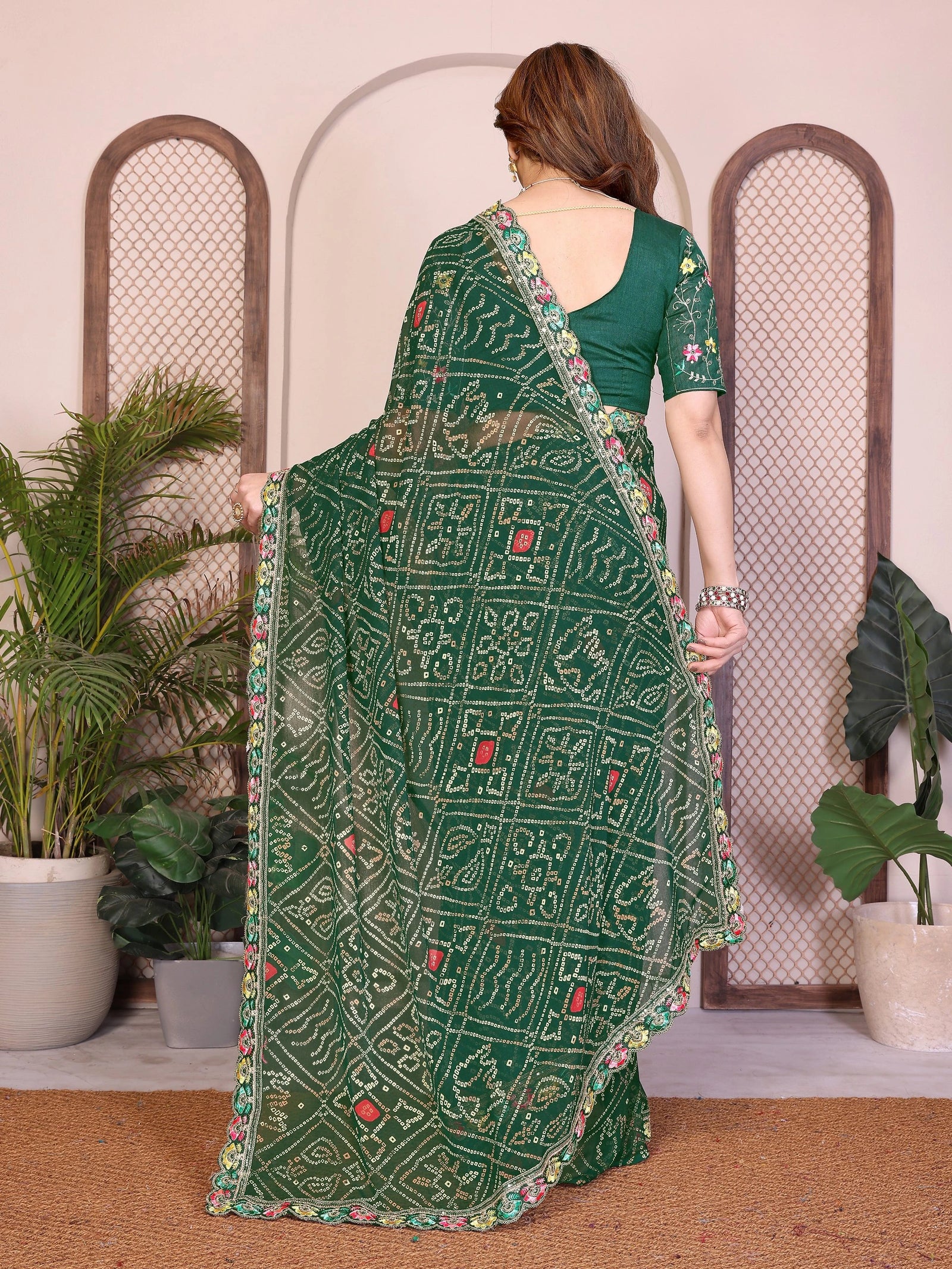 Woman wearing a green saree with intricate patterns in a decorative setting with plants.