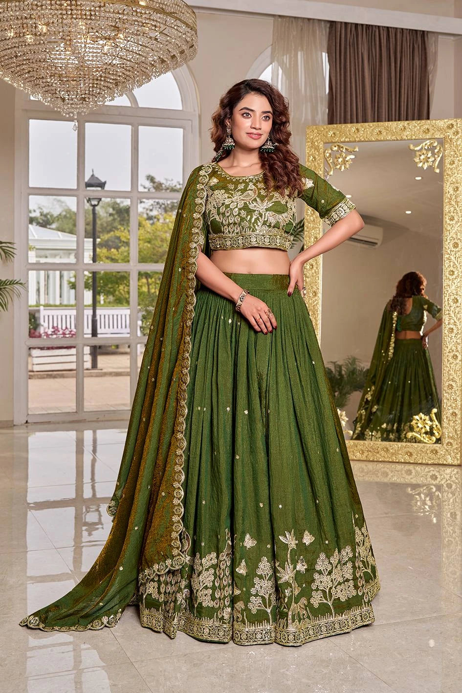 Woman in a green traditional outfit standing in a well-lit room with a mirror reflection.