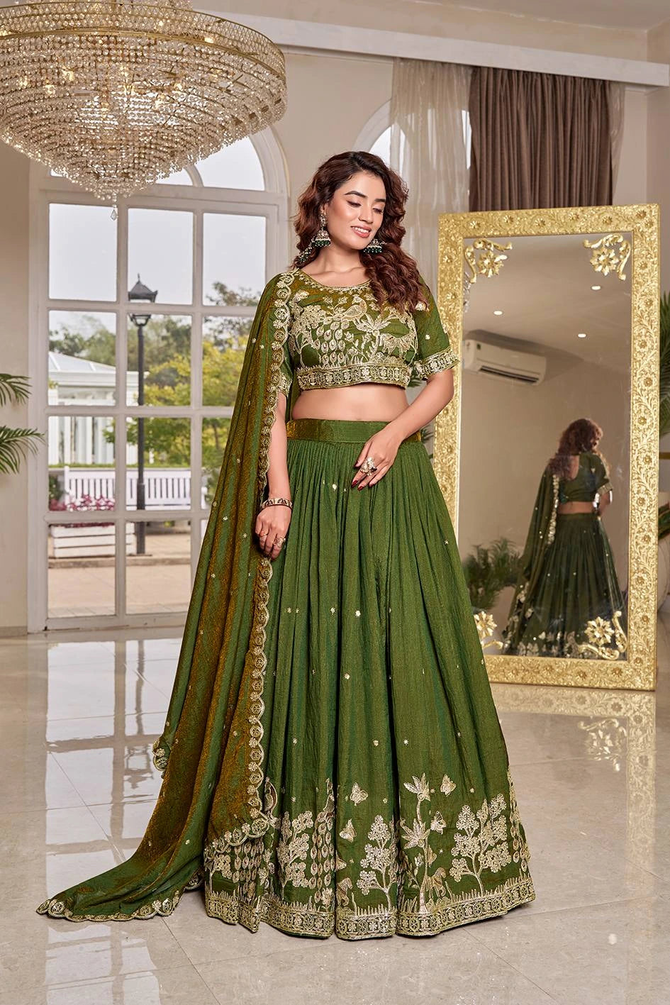 Woman in a green traditional outfit standing in a well-lit room with a mirror reflection.