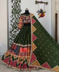 Traditional green embroidered outfit with colorful patterns on a mannequin against a white wall.