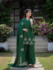 Woman in a green traditional outfit standing outdoors with flowers and a building in the background