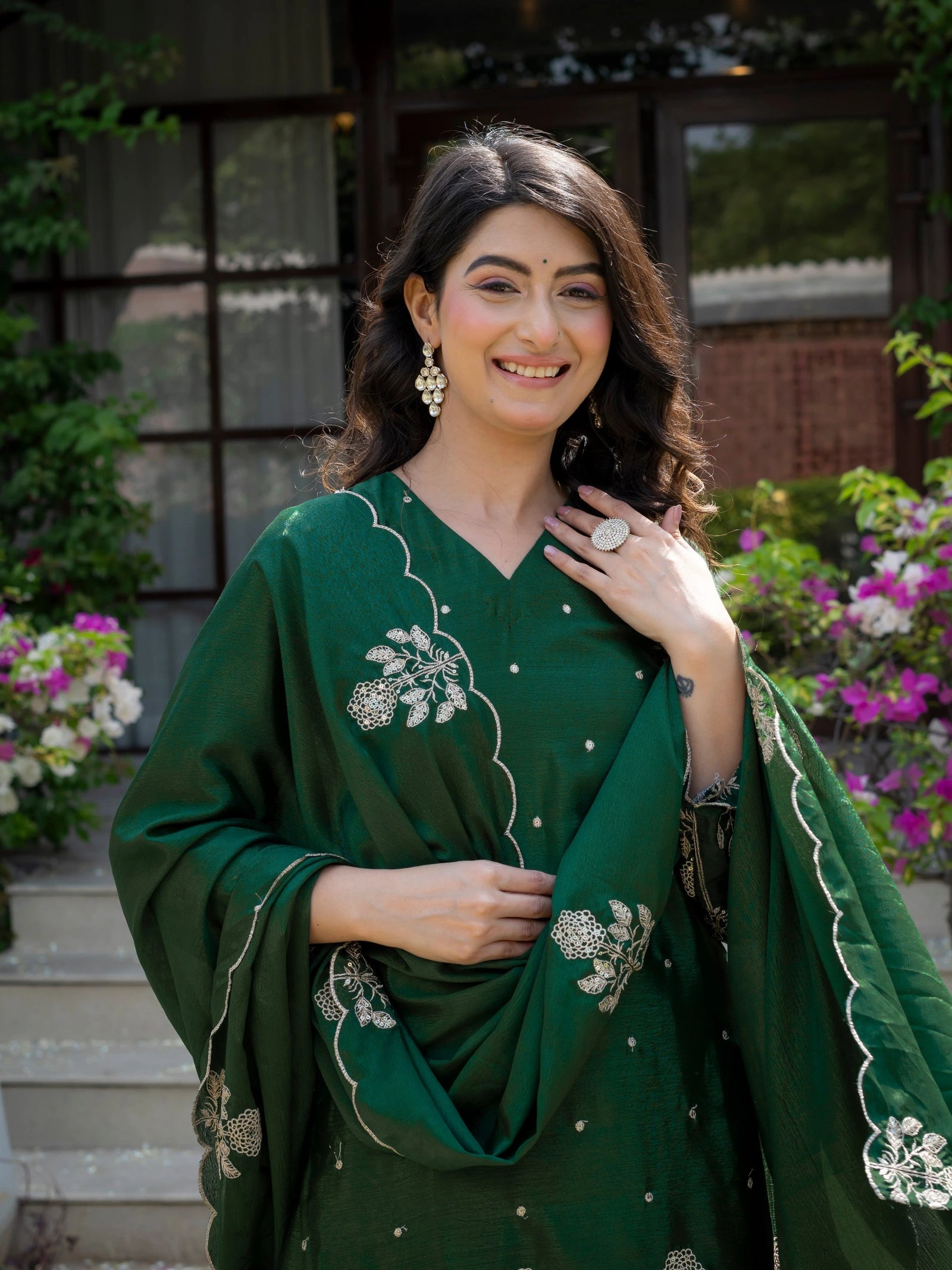 Woman in a green traditional outfit with floral patterns standing outdoors.