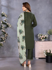 Woman wearing a green outfit with a floral scarf in a room with decorative flowers and furniture.